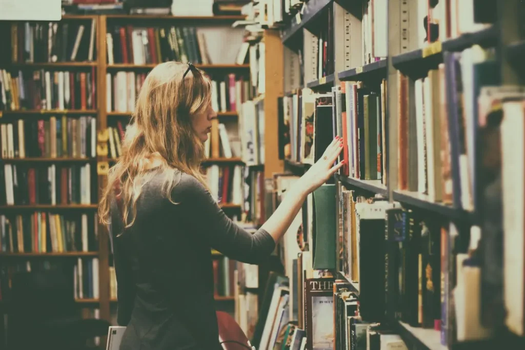 A woman browsing floor-to-ceiling bookshelves in a bookstore or library to determine how many books make a library.